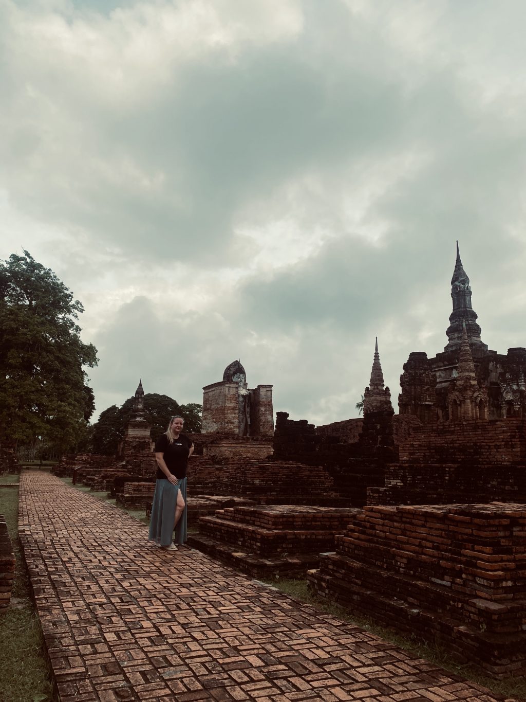 Frau steht zwischen alten Tempelruinen im historischen Park von Sukhothai, Thailand
