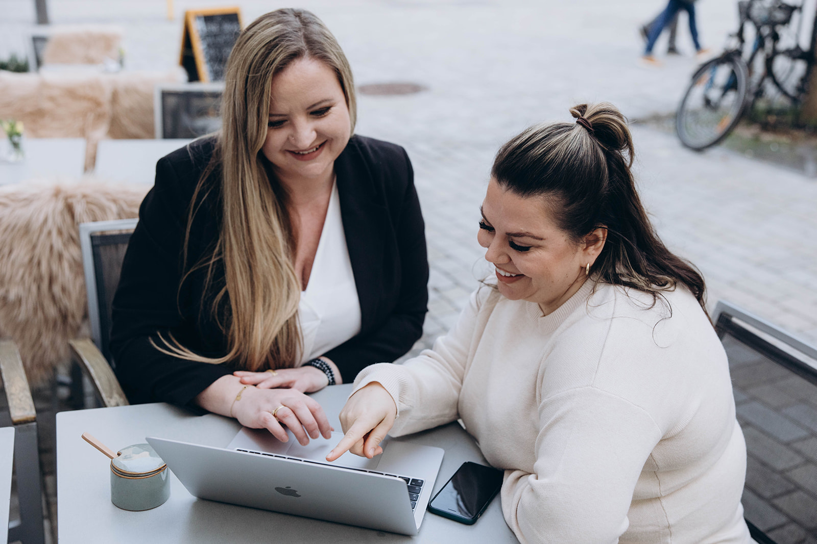 Zwei Frauen sitzen gemeinsam im Café und besprechen professionelles Webdesign auf einem Laptop.