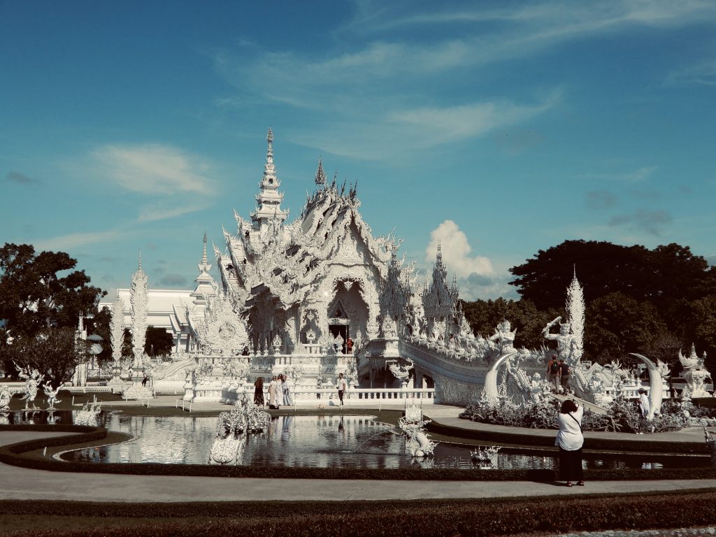 Der weiße Tempel Wat Rong Khun in Chiang Rai, Thailand, spiegelt sich im Wasser unter blauem Himmel – Symbol für Reinheit und Neubeginn.