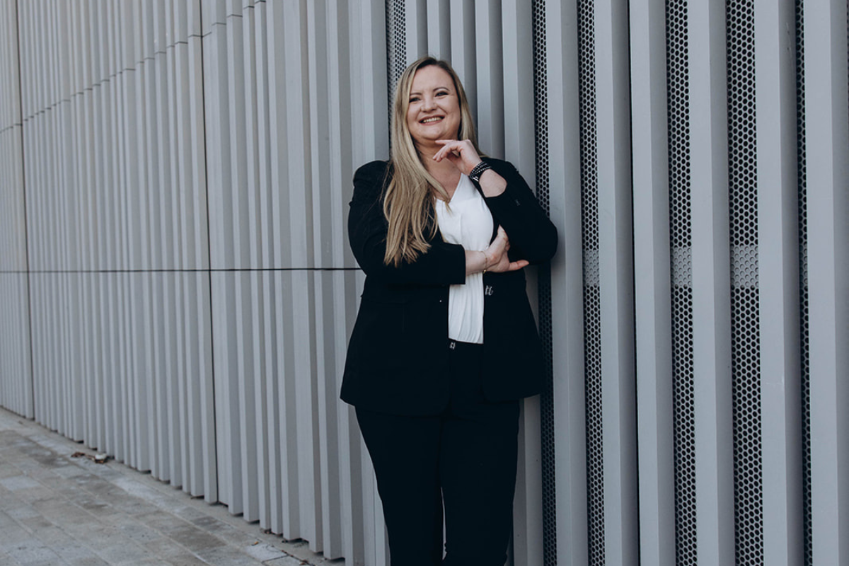 Olga Bensfar steht lächelnd vor einer modernen Fassade und repräsentiert professionelles Webdesign mit klarer Struktur und Strategie.