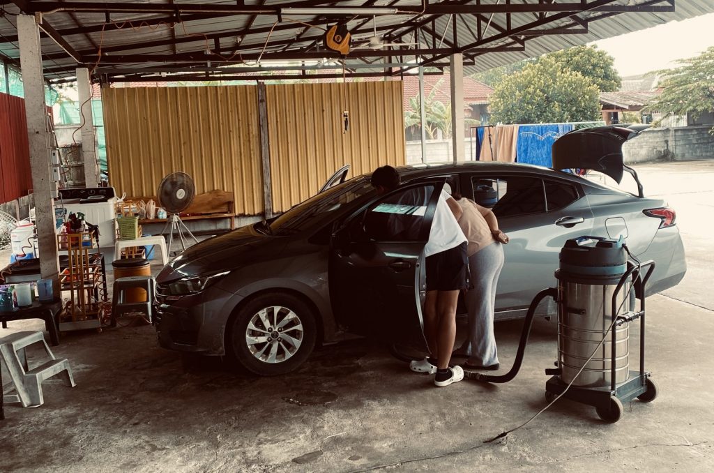 Zwei Personen reinigen ein Auto in einer offenen Werkstatt in Tak, Thailand – eine Szene, die zeigt, dass Erfolg im Business auch durch Entschleunigung und bewusste Pausen entsteht.