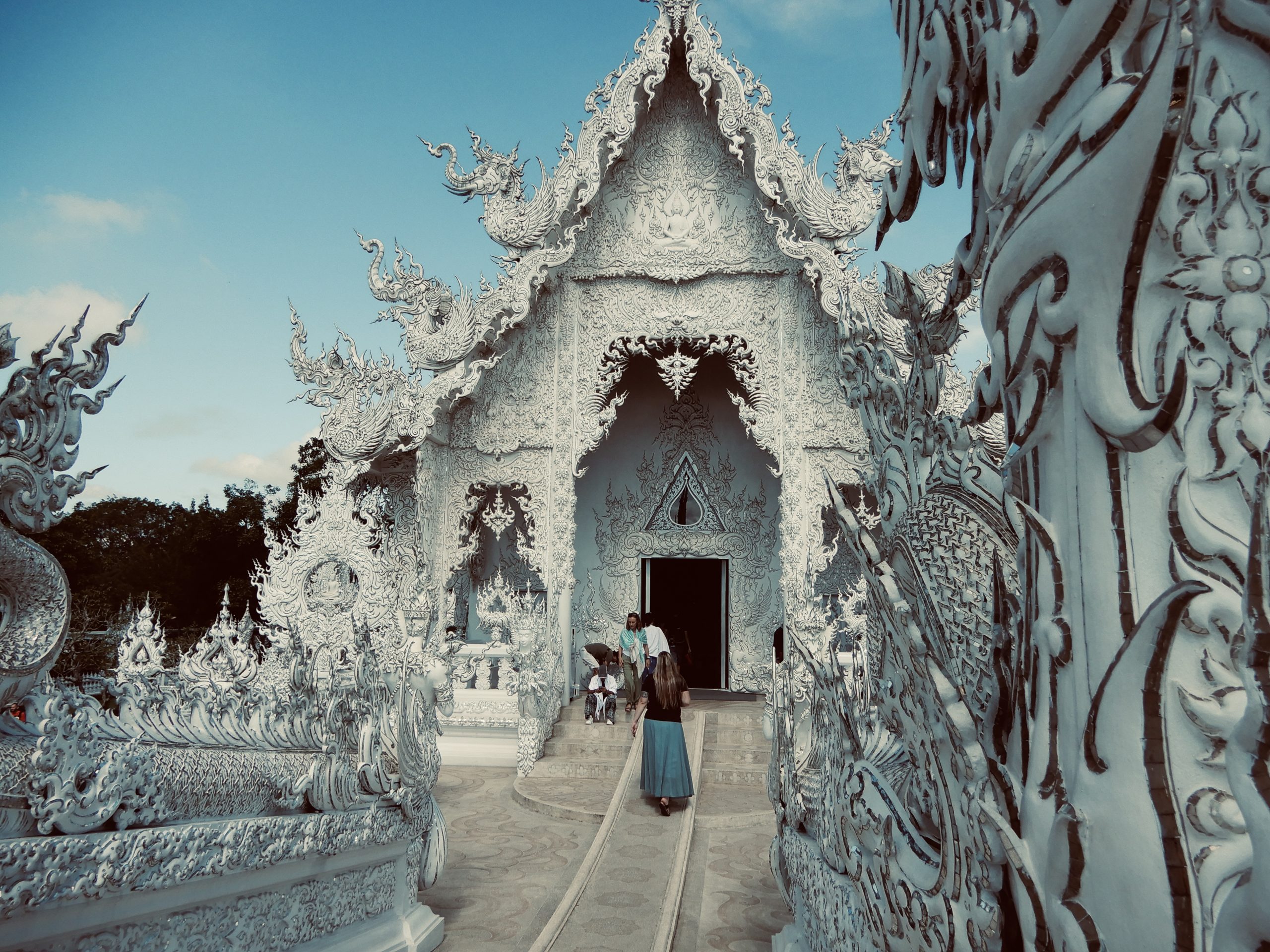 Wat Rong Khun Eingang Chiang Rai – Inspiration und digitale Freiheit im Business - Bensfar Digitale Positionierung Eingang des weißen Tempels Wat Rong Khun in Chiang Rai, Thailand, mit kunstvollen Verzierungen und Besuchern vor blauem Himmel.