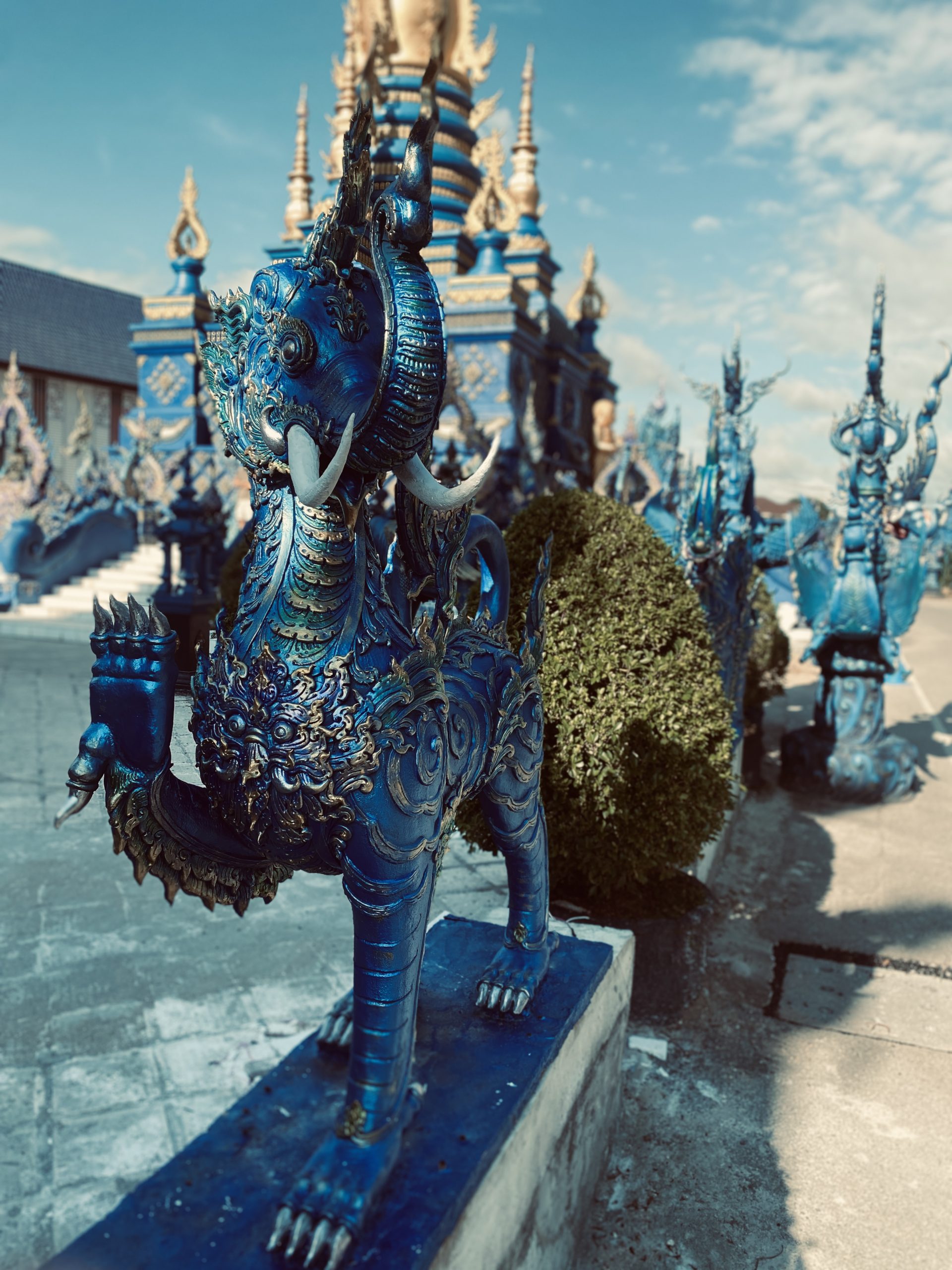 Blue Temple Chiang Rai – Digitale Inspiration und Freiheit im Business - Bensfar Digitale Positionierung Blaue Schutzstatue vor dem Blue Temple Wat Rong Suea Ten in Chiang Rai, Thailand, mit goldenen Details und leuchtendem Himmel im Hintergrund.