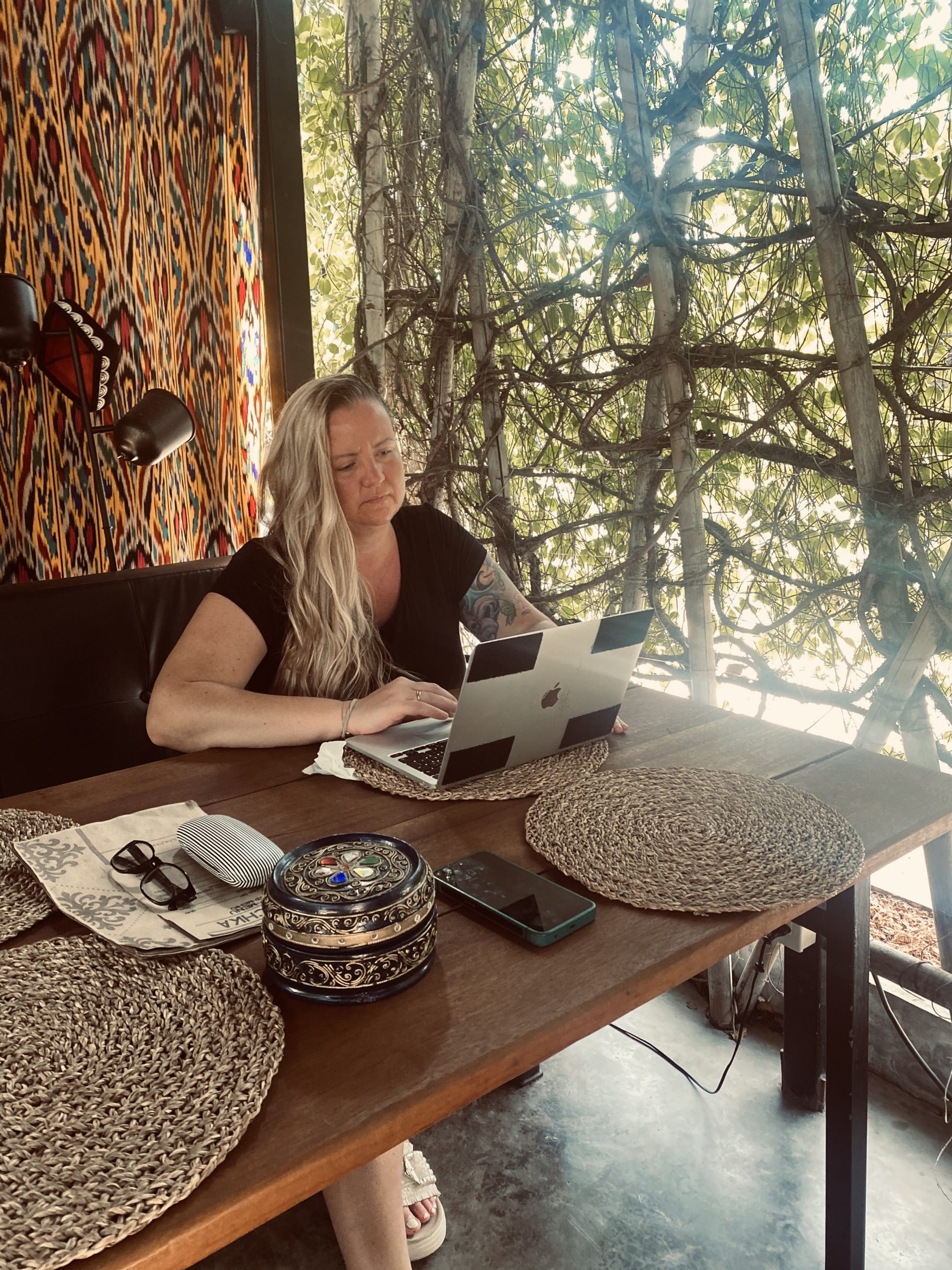 Olga Bensfar arbeitet mit Laptop in einem Café in Thailand, umgeben von tropischen Pflanzen – ortsunabhängiges Arbeiten im Ausland.